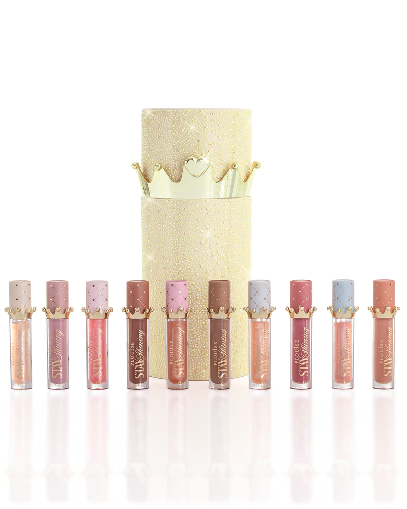 A set of ten P.Louise Christmas stay shining lip oil products arranged in a row in front of a glittery gold cylindrical lip oil box with a gold crown lid, on a clean white background.