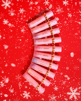 10 P.Louise Crown Stay Shining Lip Oils in Christmas scents in a row against a red background with snow effects