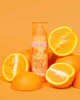 A orange bottle of P. Louise Fruity Fix Vitamin C Setting Spray with an orange background surrounded by fresh orange slices.