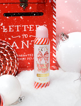 A bottle of P. Louise Ready Set Sparkle Christmas Glitter Setting Spray surrounded by festive decorations like snow, baubles and a christmas letterbox