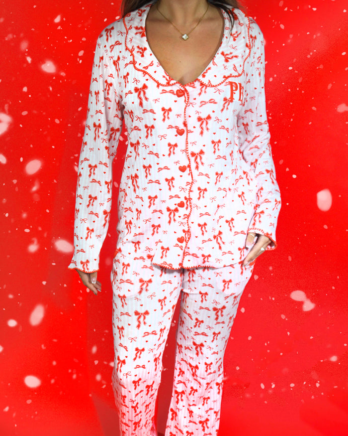 Photo du corps d'une femme portant un ensemble festif de pyjamas à rayures roses et blanches avec des motifs de nœuds rouges sur un fond rouge et des flocons de neige