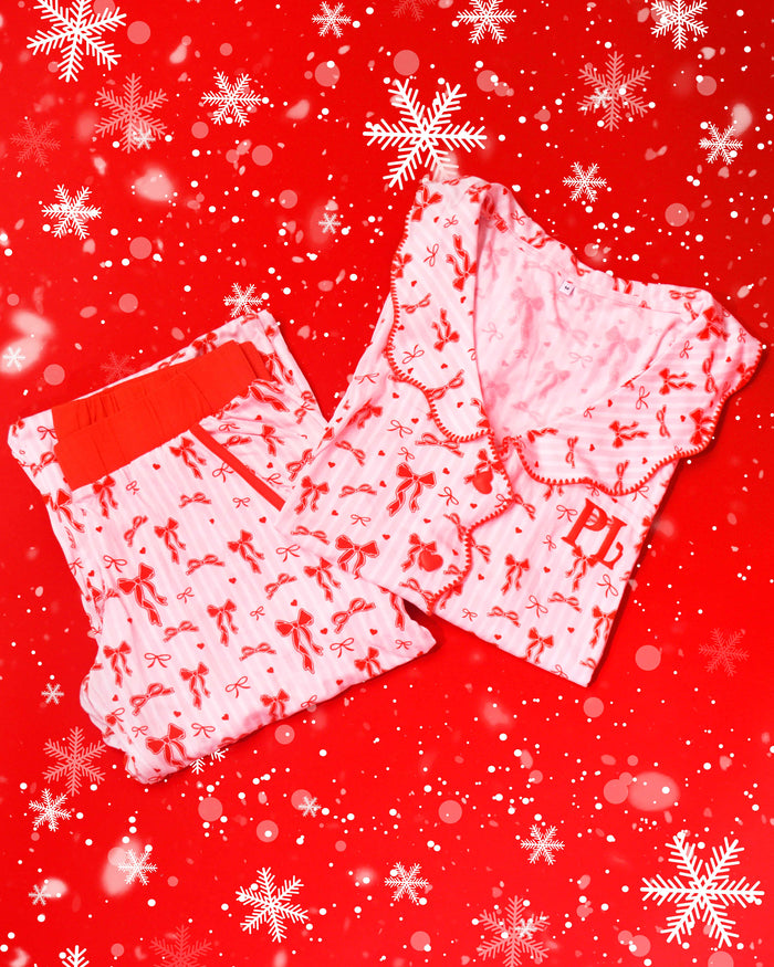 Paire de pyjamas à rayures roses et blanches avec des motifs de nœuds festifs rouges sur fond rouge avec des flocons de neige
