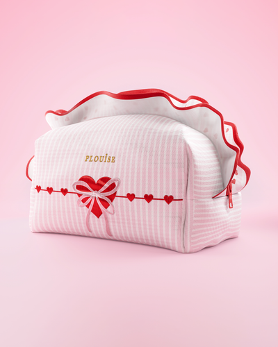 Une trousse de maquillage et de soin P.Louise à rayures roses et blanches avec des volants et un motif cœur d'amour sur fond rose