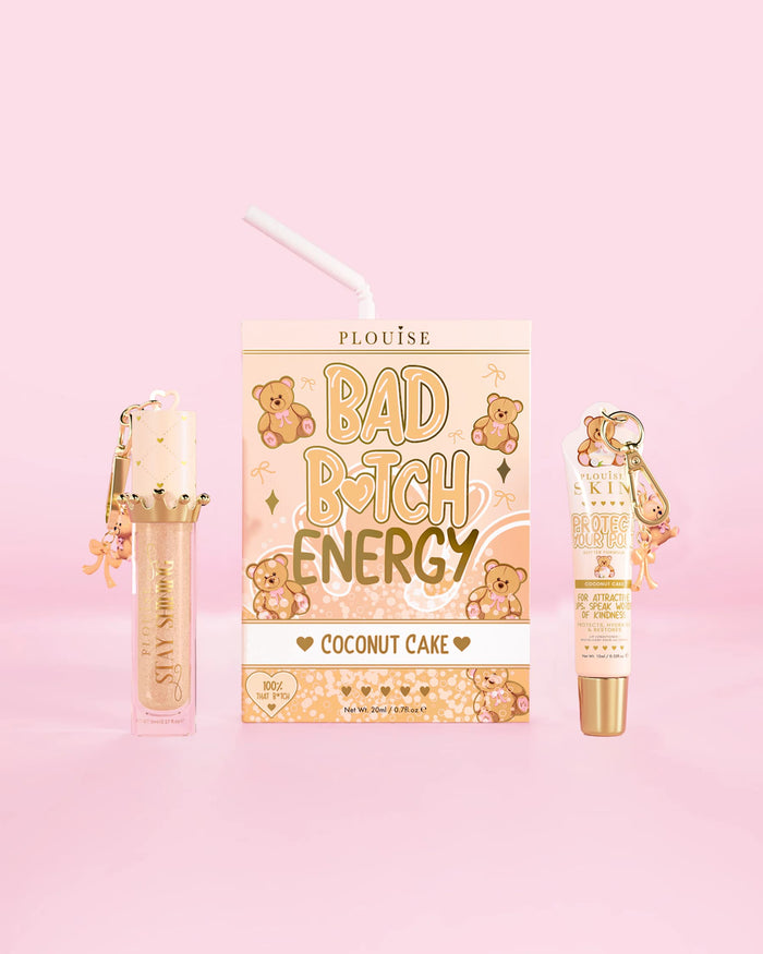 Un duo pour les lèvres P.Louise Teddy Glitter Bad Bitch Energy au parfum de gâteau à la noix de coco comprenant un revitalisant pour les lèvres et une huile pour les lèvres sur un fond rose