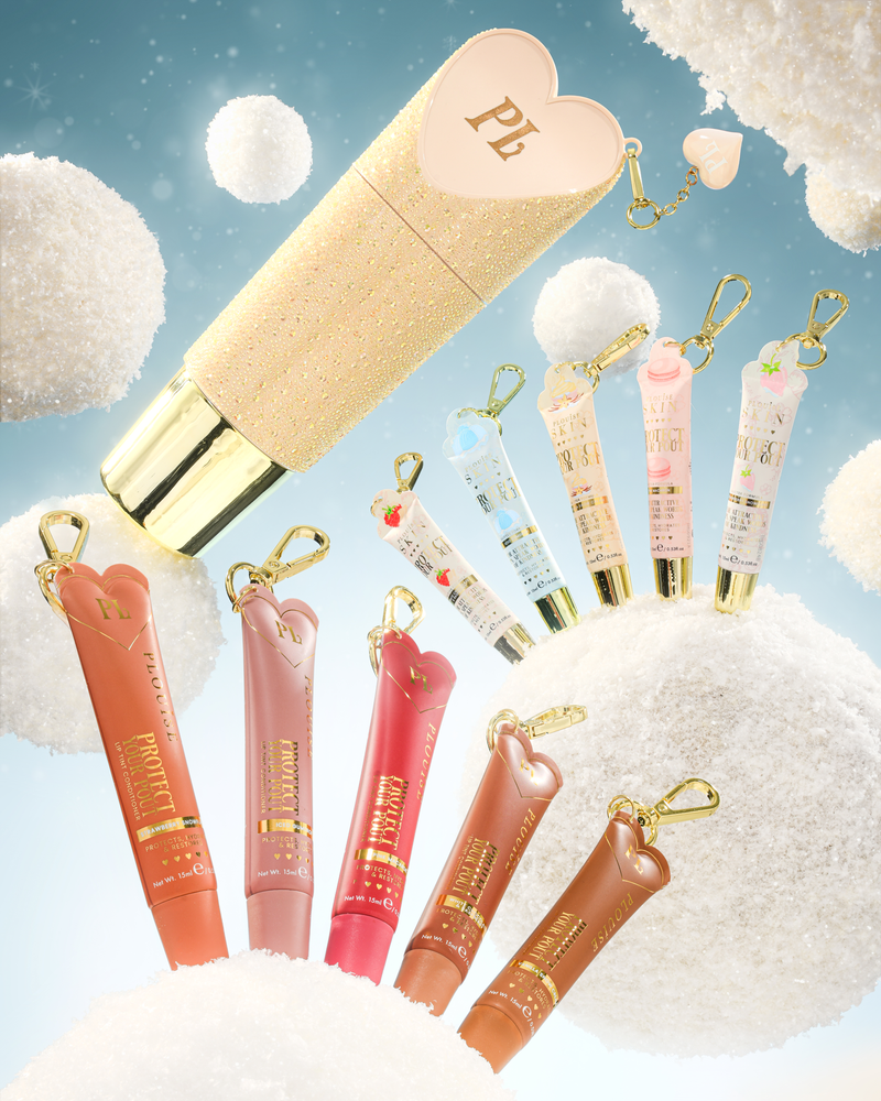 A set of heart-shaped lip conditioner keychain tubes with gold keychains, displayed against a whimsical background of fluffy white clouds and a light blue sky. The set includes a large gold glitter tube with a pink heart cap, several smaller lip gloss or cream tubes in peach, pink, red, and brown shades, and smaller pastel blue and pink keychains.