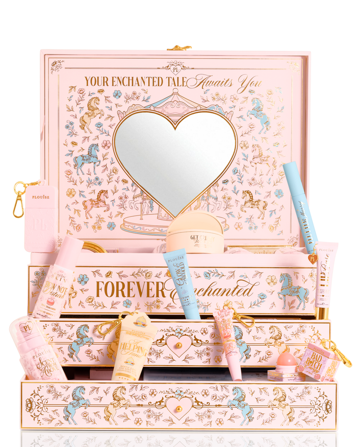 Un coffret cadeau beauté PR de Noël rose pastel, bleu et jaune P.Louise étiqueté « Your Enchanted Tale » avec un miroir en forme de cœur sur le couvercle et des tiroirs ouverts, entouré de tubes cosmétiques assortis, de bouteilles et d'une petite pochette sur fond blanc.