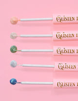 5 eye-liners pailletés P.Louise Glisten To Your Heart alignés avec une goutte de produit au bout sur fond rose