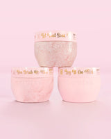 Trois contenants roses P.Louise Hop Into Self-Care Pink Marshmallow contenant des sels de bain, un gommage corporel et du beurre corporel avec un texte doré sur fond rose