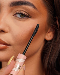 Gros plan d'une baguette de mascara P.Louise Tearproof tenue près de l'œil d'une personne avec un arrière-plan flou