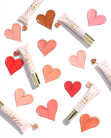 Three tubes of P.Louise Lip Base in shades of pink, coral, and peach, arranged on a white background with matching heart-shaped lip swatches and small heart charms.