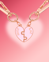 A rose gold split heart keychain with two interlocking puzzle halves engraved with 'BESTIE' and '&ME', attached to matching carabiners against a pink gradient background.