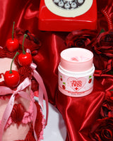 Un récipient de baume nettoyant de maquillage P.Louise Plot Twist Make It Melt affiché sur une surface en tissu rouge avec des éléments décoratifs dont une cerise et un téléphone rouge vintage en arrière-plan.