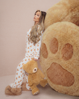 Femme en pyjama en peluche tenant un ours en peluche à côté d'une grande patte d'ours en peluche sur fond beige