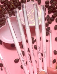 Une collection de crayons à sourcils roses P.Louise avec des pinceaux spoolie, présentés aux côtés de grains de café et d'un plat rose.