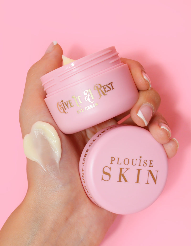 Une personne tenant un pot rose de crème pour les yeux P.Louise Give It A Rest sans le couvercle, affichant le nom du produit et la marque sur le pot.