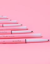 Une collection de mini crayons à sourcils P.Louise disposés en rangée avec le nom de la marque visible sur le corps des crayons, affiché sur fond rose