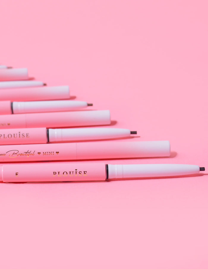 Une collection de mini crayons à sourcils P.Louise disposés en rangée avec le nom de la marque visible sur le corps des crayons, affiché sur fond rose